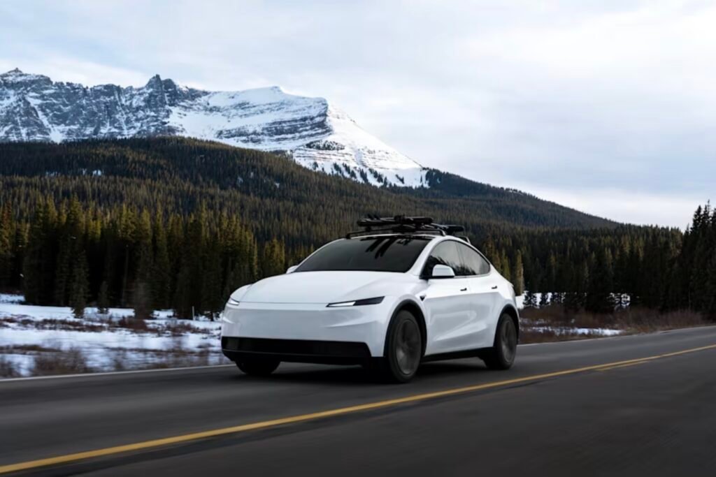 Valkoinen Tesla Model Y ajaa vuoristomaisemassa lumihuippuisen vuoren edustalla