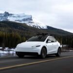 Valkoinen Tesla Model Y ajaa vuoristomaisemassa lumihuippuisen vuoren edustalla